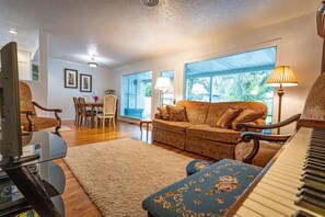 A living room with a piano, a sofa, a dining table with chairs, and large windows. - 10-Min Walk to Downtown & Lake • 10-Min Drive to Schweitzer Base (Sandpoint)