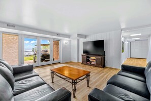 Una sala de estar moderna con televisor de pantalla plana, sofás de cuero, una mesa de centro de madera y un ventanal corredizo que da a un balcón.