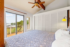 A bedroom with a large bed, a ceiling fan, a view of a lake, and a balcony.