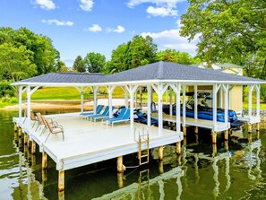 A covered dock with lounge chairs and a boat.