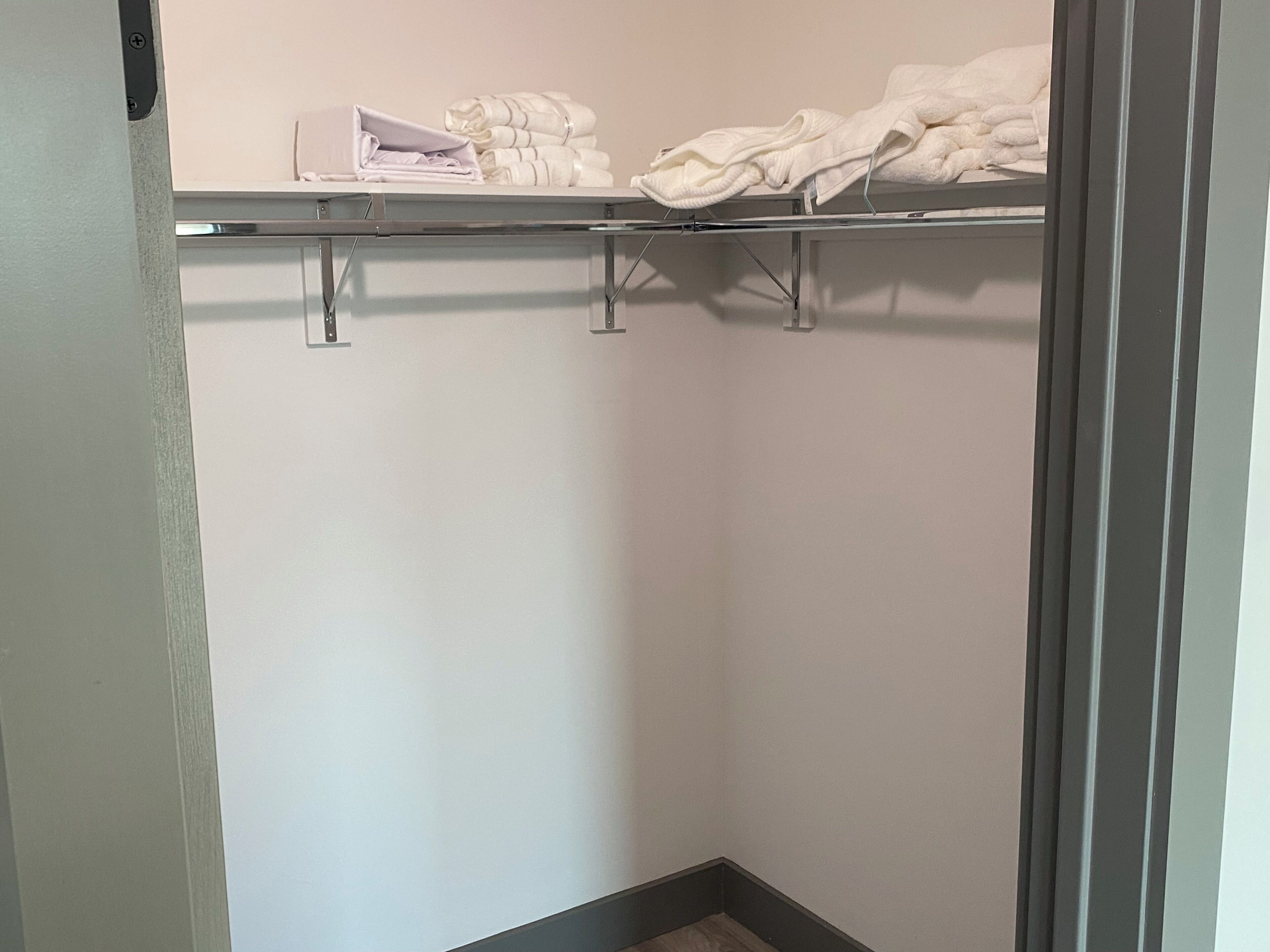 Un dressing ouvert avec une étagère en métal où sont pliés des serviettes et un vêtement.