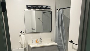 Un baño con inodoro, lavamanos, espejo y cabina de ducha.