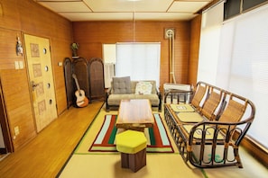 A room with a sofa, a small table, a wicker chair, a guitar, and a window with blinds.