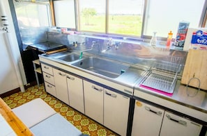 A kitchen with two stainless steel sinks, a window with a view of greenery, and various kitchen items on the counter.