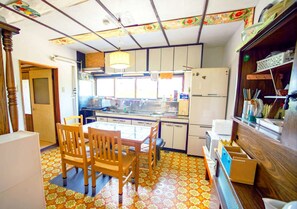 A compact kitchen with a dining area, featuring a patterned floor, wooden chairs, and a refrigerator. - スキー場まで15分！一棟貸切！最大7人！エアコン付！ファミリー向け！ (空知郡上富良野町)