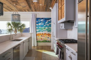 Una cocina moderna con techo de madera, armarios blancos, estufa de acero inoxidable y un mural de playa en la pared.