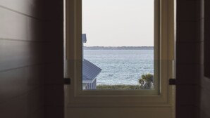 A window with a view of a body of water and a distant shoreline. - New Stunning Luxury Beach Home with Private Pool! (Pensacola Beach)