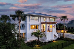 A modern two-story house with a balcony, a covered porch, and a well-maintained lawn. - New Stunning Luxury Beach Home with Private Pool! (Pensacola Beach)