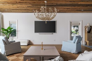 Ein Wohnzimmer mit Holzbalkendecke, einem Flachbildfernseher, zwei karierten Sofas, einem Couchtisch und einer großen Pflanze.
