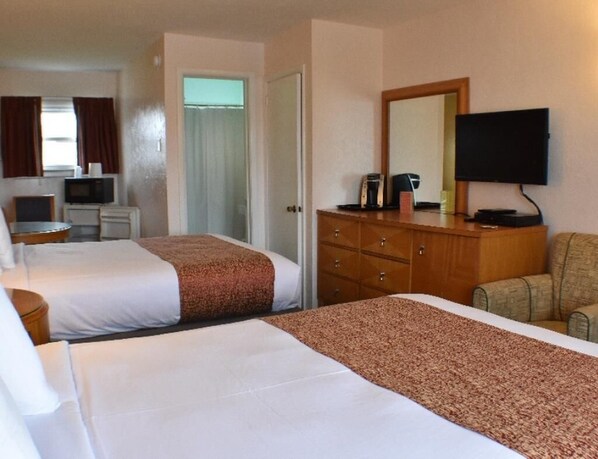 A hotel room with two beds, a television, a desk with a computer, and a chair.