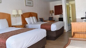 Ett hotellrum med två sängar, ett skrivbord, en stol och en dörr som leder till ett annat rum.