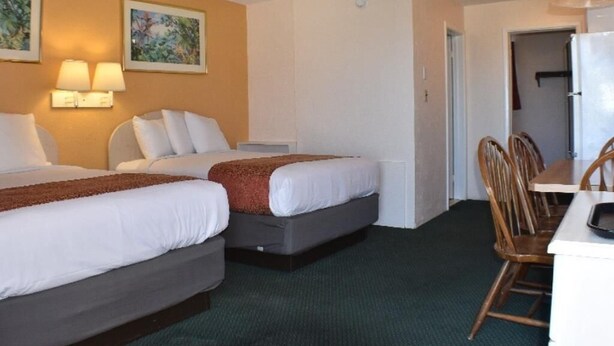 Ett hotellrum med två sängar, ett matbord, stolar, ett kylskåp och väggmonterade lampor.