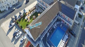 En vy från ovan av ett hotell med en swimmingpool, ett takförsett utomhusområde och en parkeringsplats.