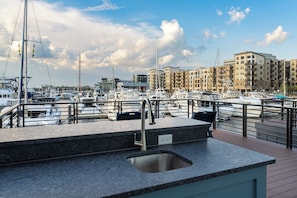A marina with boats docked, a building labeled 'MARINA GRILL,' and a modern outdoor kitchen area with a sink. - Sol at The Cove Riverwalk Villas (Wilmington)