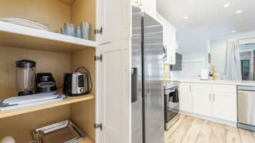 A modern kitchen with white cabinetry, stainless steel appliances, and wooden flooring.