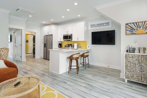 A modern kitchen with white cabinetry, a stainless steel refrigerator, a microwave, and a bar area with two stools. - Sol at The Cove Riverwalk Villas (Wilmington)