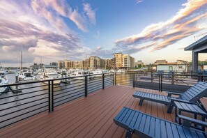 Un puerto deportivo con barcos amarrados, una terraza de madera con sillones de descanso y edificios al fondo.