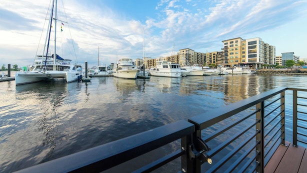 Un puerto deportivo con varias embarcaciones amarradas, un paseo marítimo y edificios residenciales modernos al fondo.