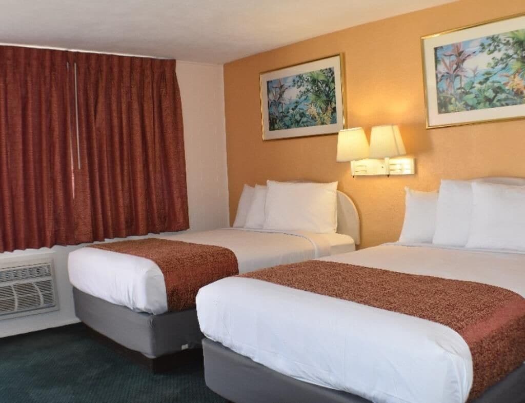 A hotel room with two beds, a heater, two wall-mounted lamps, and two framed pictures on the wall.