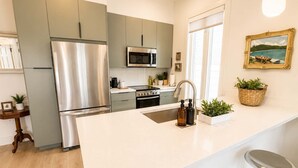 Una cocina moderna con un refrigerador, un microondas y un horno de acero inoxidable. Hay una isla grande con un lavamanos y taburetes de bar.