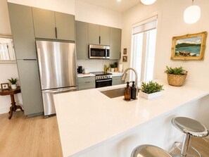 Eine moderne Küche mit Edelstahl-Kühlschrank, Mikrowelle und Backofen. Eine große Kücheninsel mit Spüle und Barhocker ist ebenfalls vorhanden.