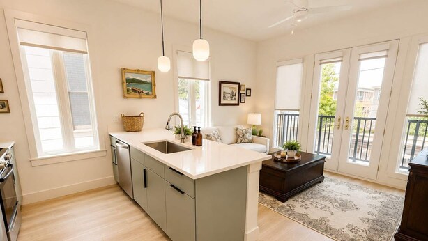 Una cocina moderna con una isla central, un comedor con mesa de madera oscura y vistas al exterior a través de grandes ventanales.