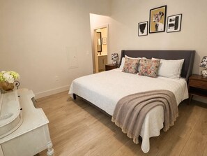 A bedroom with a bed, nightstands, a dresser, and a door leading to another room. - The Jardin Birch Suite | Near Downtown (Savannah)