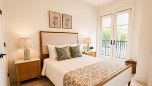 Un dormitorio con cama, dos mesitas de noche, un ventanal y una puerta.