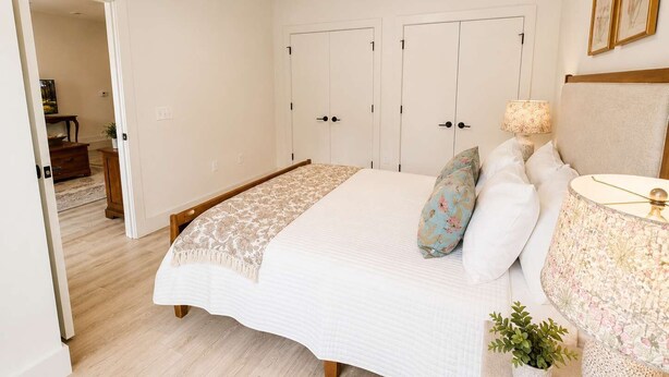Un dormitorio con cama, lámparas de noche, una mesita de noche y una puerta que da a otra habitación.