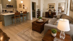 Una sala de estar moderna con un sofá, una mesita de centro y un comedor con sillas, y una cocina al fondo.