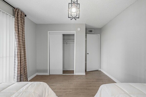 A bedroom with two beds, a closet, and a window with curtains. - 1307-Wilcrest-4201 (Houston)