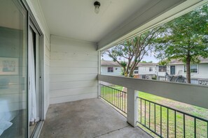A covered balcony with a metal railing, a concrete floor, and a view of neighboring houses and trees. - 1307-Wilcrest-4201 (Houston)
