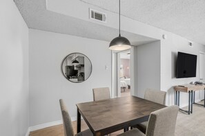 A dining area with a wooden table, chairs, a pendant light, a round mirror, and a TV on the wall. - 1307-Wilcrest-4201 (Houston)