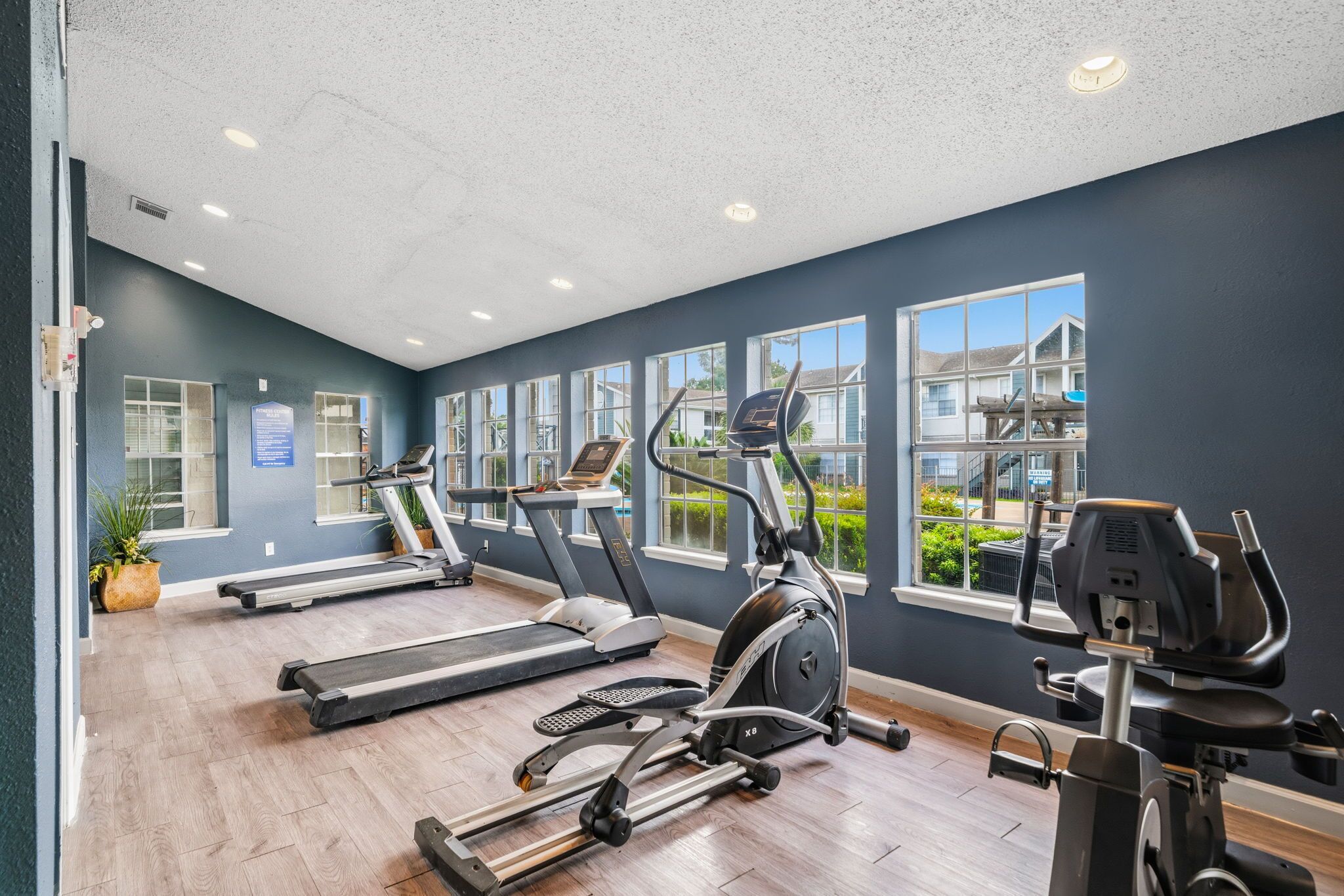 Une salle de sport équipée de tapis de course, d’un vélo elliptique et d’un vélo d’appartement, avec de grandes fenêtres donnant sur l’extérieur.