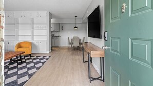 Uma cozinha moderna com armários brancos, uma área de refeições com tapete quadriculado e uma porta verde.