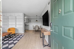 A modern kitchen with white cabinets, a dining area with a checkered rug, and a green door. - 1307-Wilcrest-4201 (Houston)