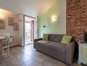 Un salon avec un canapé marron, des coussins verts, une table blanche avec une chaise et un mur en briques.