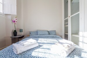 Ein Schlafzimmer mit einem Bett, Kissen, einem Nachttisch, einer Lampe und einer Topforchidee.
