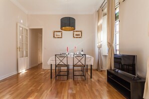 Ein Essbereich mit einem Tisch für vier Personen, einem Fernseher und einem großen Fenster mit Vorhängen.