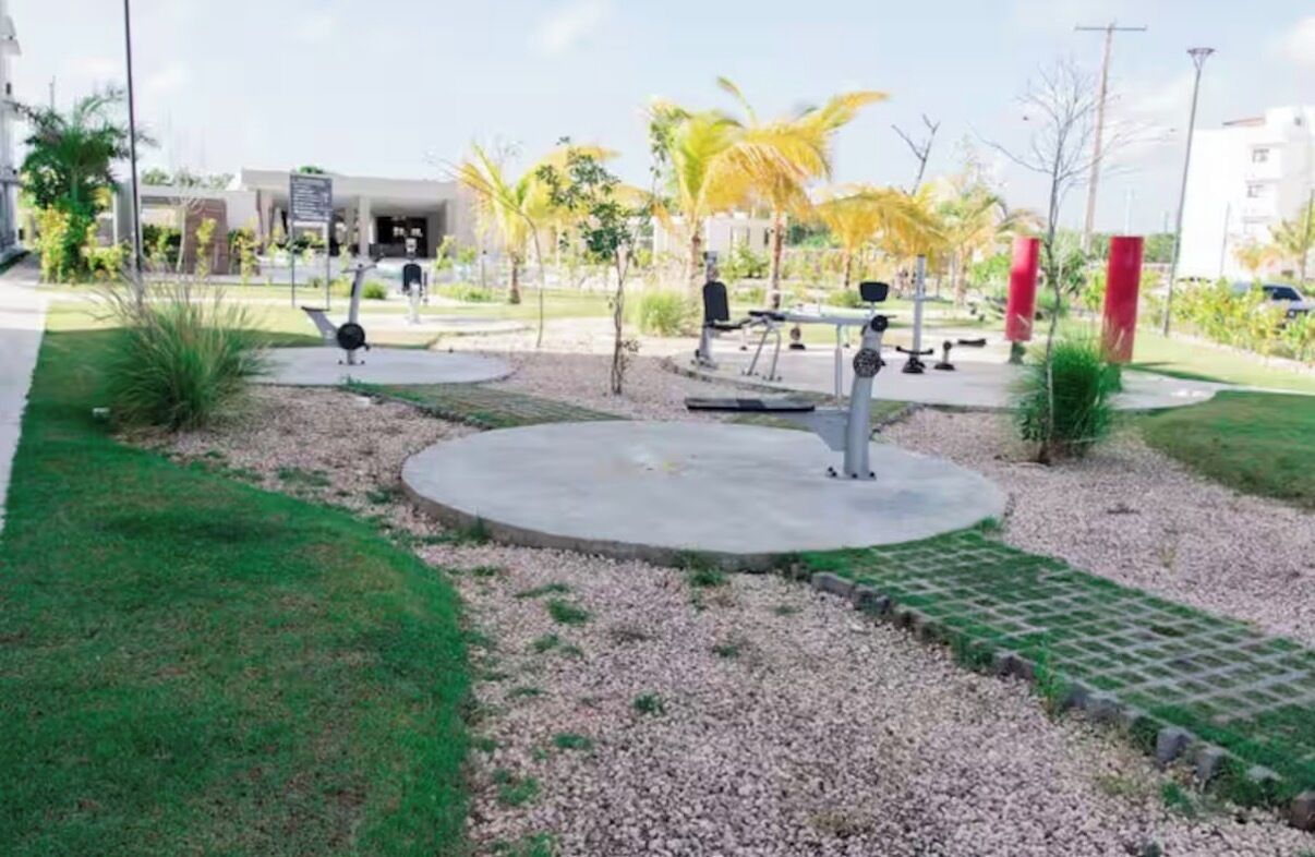 Un'area esterna curata con attrezzature per esercizi, una zona salotto circolare e un edificio sullo sfondo.