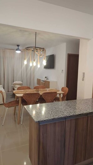 A modern kitchen with a granite countertop, wooden cabinets, and a dining area with wicker chairs. - Cozy 2-bedroom apartment with AC in Punta Cana 2 mins from downtown (Punta Cana)