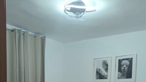 Una camera da letto con un letto, una lampada a sospensione, una finestra con tende e due quadri appesi al muro.