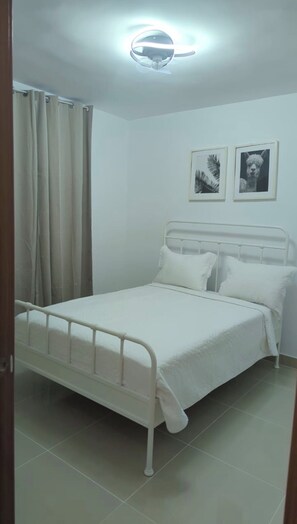 A bedroom with a bed, a ceiling light, a window with curtains, and two framed pictures on the wall. - Cozy 2-bedroom apartment with AC in Punta Cana 2 mins from downtown (Punta Cana)