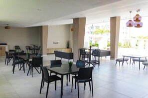 A spacious indoor dining area with multiple tables and chairs, a reception desk, and large windows offering a view of the outdoors. - Cozy 2-bedroom apartment with AC in Punta Cana 2 mins from downtown (Punta Cana)