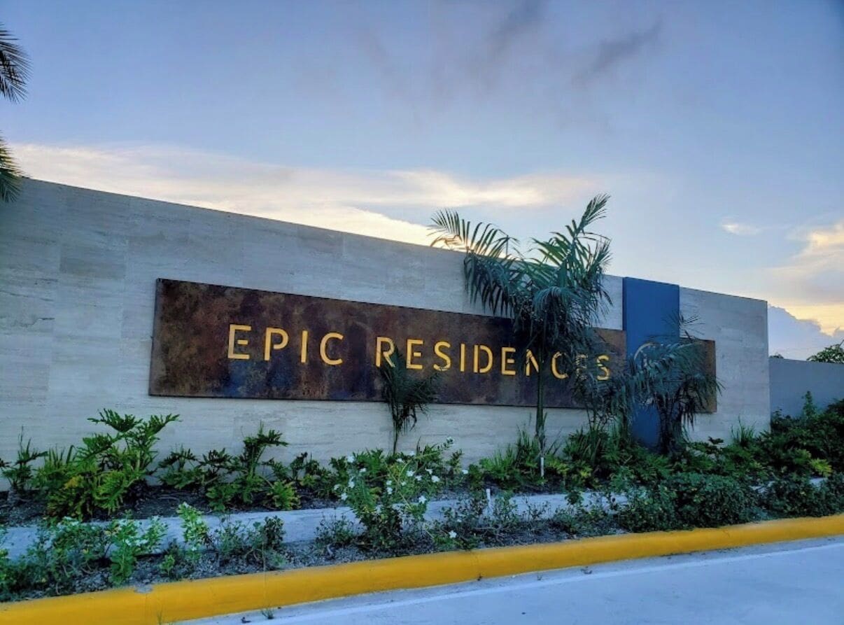 Señalización para 'EPIC RESIDENCES' con diseño moderno, acompañada de vegetación y cielo despejado.