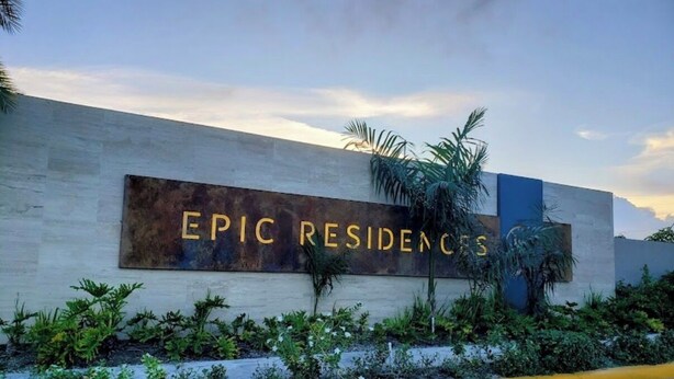 Segnaletica per 'EPIC RESIDENCES' dal design moderno, con vegetazione e cielo sereno.