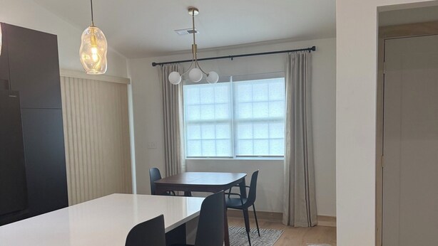 Ett modernt kök med en vit bänkskiva, svarta stolar och en hängande lampa.