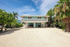 A two-story beachfront property with a covered porch and a flag.