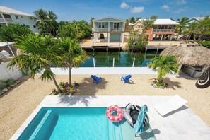 A pool area with a clear blue pool, two blue lounge chairs, and a thatched-roof structure.