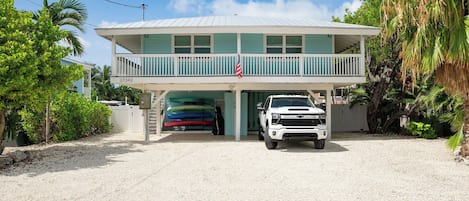 A two-story building with a covered garage, a white pickup truck parked in front, and a row of colorful kayaks inside the garage.